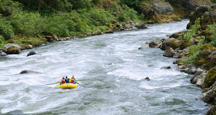 Balsa inflable amarilla con un pequeño grupo haciendo rafting en aguas bravas por un río de montaña boscoso.
