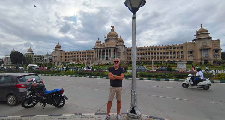 Hombre parado con un gran edificio de fondo a lo largo de una calle concurrida.