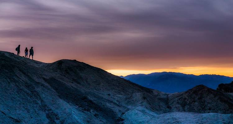 Silhouetten van wandelaars op een bergkam onder een kleurrijke zonsondergang.