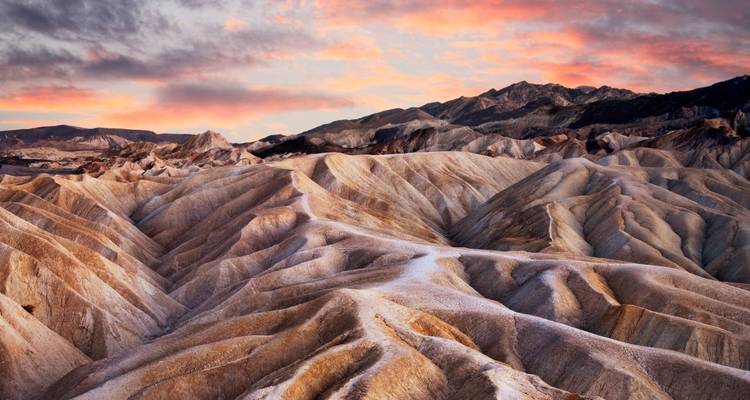 Uitgestrekt woestijnlandschap met dramatische rotsformaties en een kleurrijke hemel.