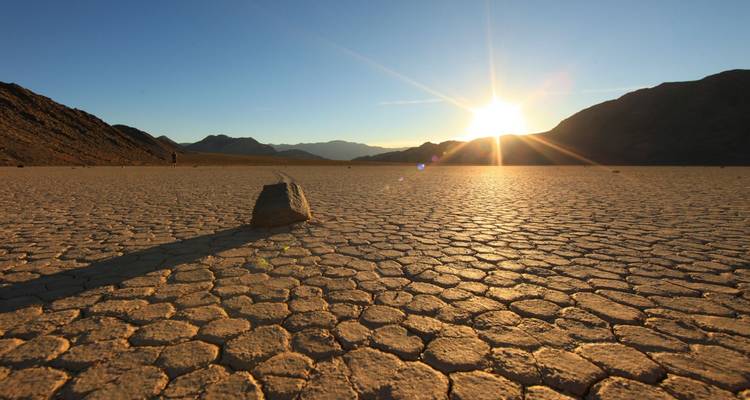 Woestijnlandschap met een enkele rots en de zon die ondergaat achter bergen.