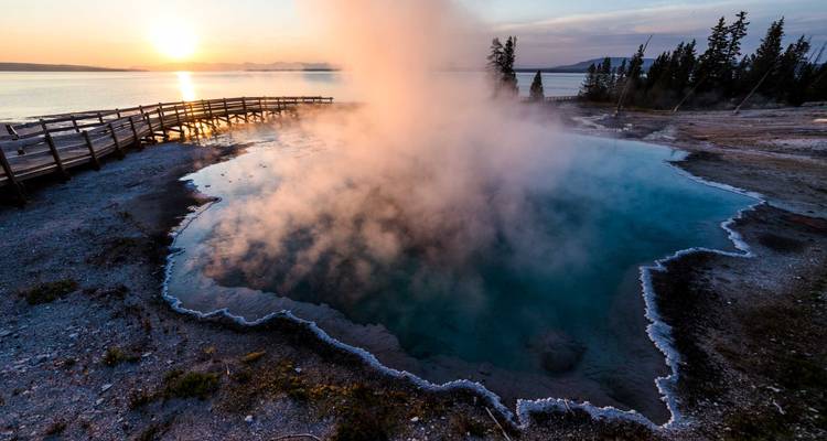 Hot spring in Yellowstone with steam rising during sunset.