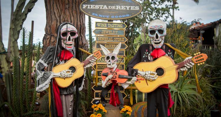 Skeleton figures playing guitars at a fair with signs.