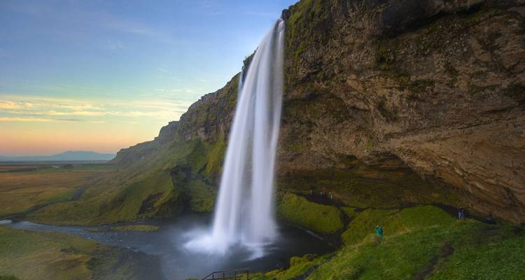 Seljalandsfoss waterfall with lush green surroundings at sunset.