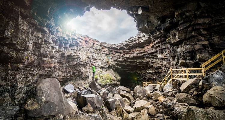 Een persoon die in een grote rotsgrot staat met licht dat naar binnen filtert.