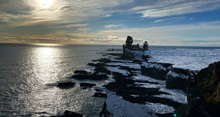 Een dramatisch kustlandschap met sneeuw en oceaan onder een ondergaande zon.