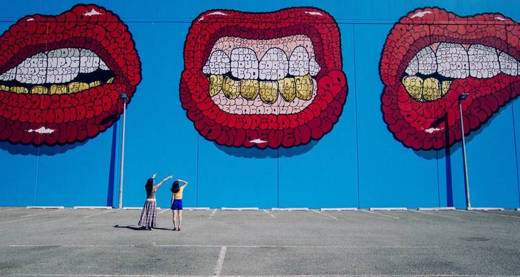 Two people observing a large mural on a building.