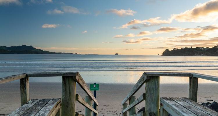 Des marches en bois menant à une plage sereine avec un océan calme et des nuages dans le ciel.