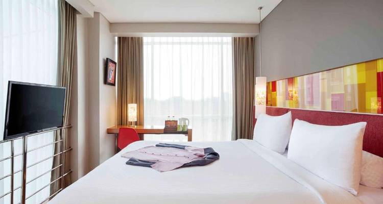 Modern hotel room with a comfortable bed and large window.