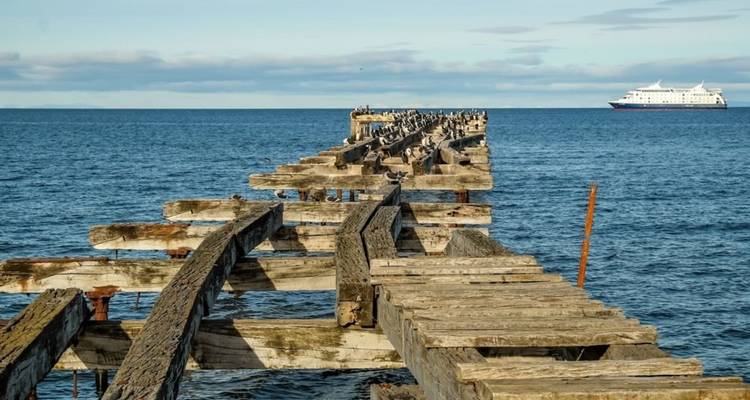 Ein hölzerner Steg, der ins Meer hinausführt, mit einem Schiff in der Ferne.