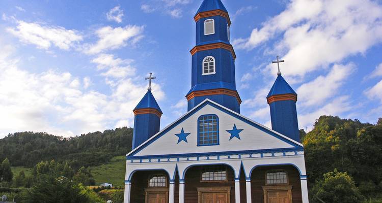 White and blue church with star decorations in front of a hillside.
