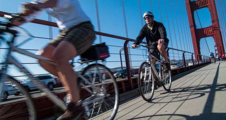 Radfahrer fahren über die Golden Gate Bridge mit Hängeseilen und blauem Himmel darüber.
