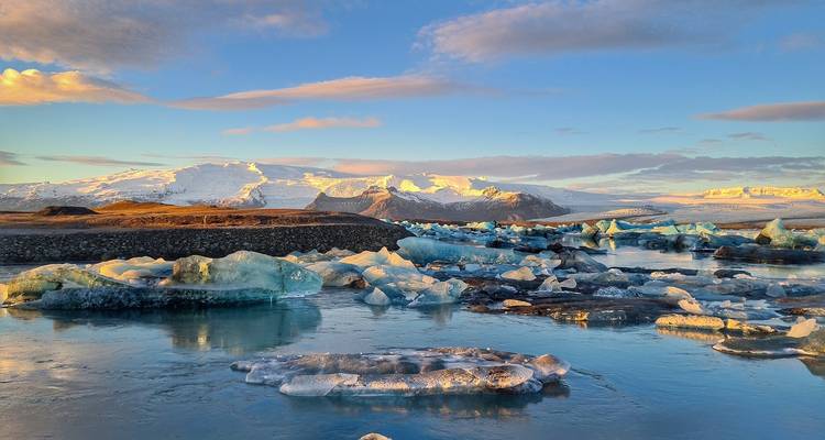 Icebergs flottant dans un lagon serein avec des montagnes en arrière-plan.