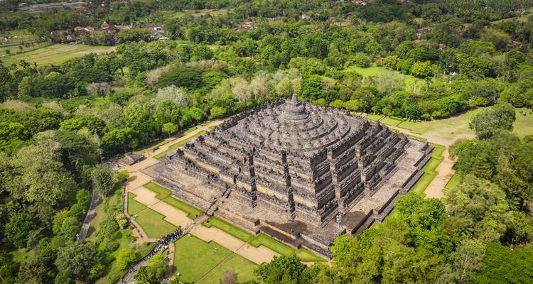 Drone view of the massive stone tiers of Borobudur Temple surrounded by dense green jungle.