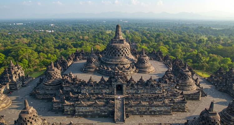Symmetrical aerial view of Borobudur's central stupa rising above surrounding terraces amid lush forest.