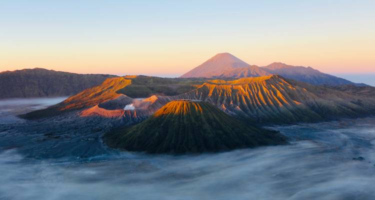 Sunrise casts golden light on the craters and ridges of Mount Bromo within a mist-filled caldera.