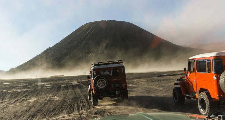 Dusty jeeps drive across the volcanic sands toward Mount Bromo under clear skies.