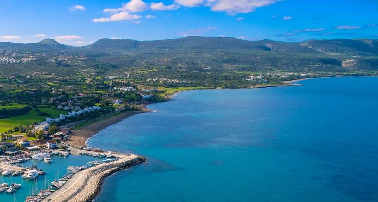 Aerial view of a coastline with a marina and hilly landscape.