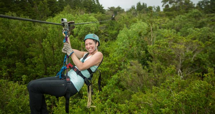 Glimlachende vrouw in harnas glijdt langs een jungle zipline hoog boven het groene bladerdak.