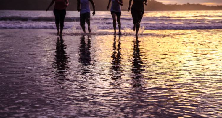 Silhouetten van mensen die tijdens zonsondergang langs het strand rennen.
