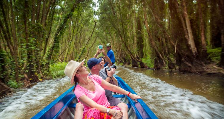 Les voyageurs traversent rapidement un canal forestier inondé dans un bateau à moteur bleu, prenant des photos tandis que l'eau laisse des traces derrière.