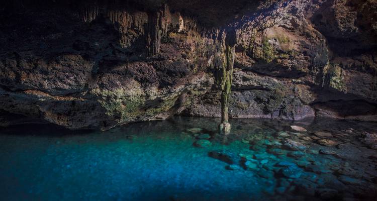Agua azul cristalina dentro de un cenote subterráneo con estalactitas.