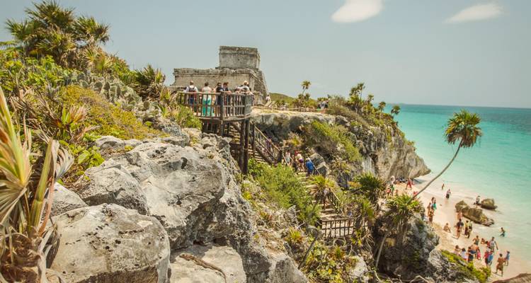 Icónicas ruinas mayas en lo alto de los acantilados de Tulum con vistas a las aguas turquesas del Caribe y a los bañistas ocupados abajo.