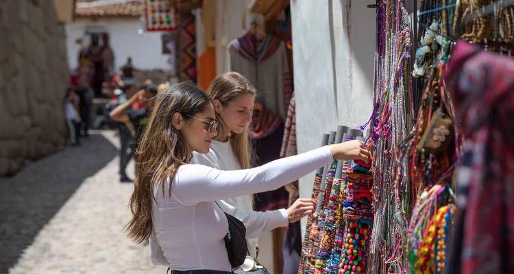Dos mujeres exploran coloridos textiles hechos a mano en un mercado callejero andino con adoquines
