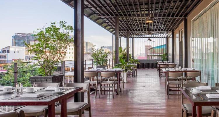 Outdoor dining area on a balcony with tables, chairs, and cityscape views.