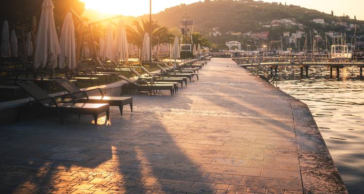 Las tumbonas vacías proyectan largas sombras en el paseo marítimo al atardecer.