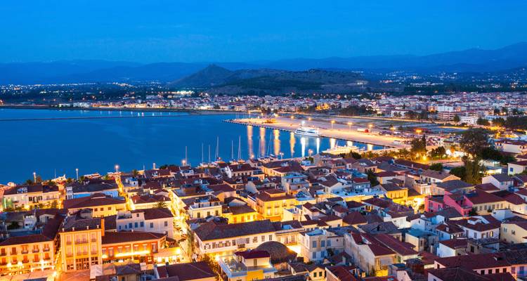 Aerial view of a coastal city at night with lit buildings and a bay.