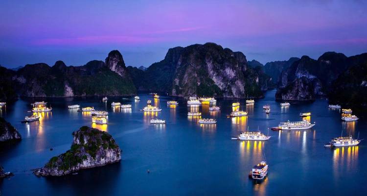 Evening scene at Halong Bay with illuminated boats and limestone formations.