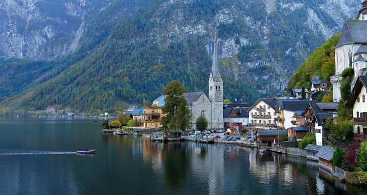 Un village au bord du lac avec un clocher d'église et des montagnes.