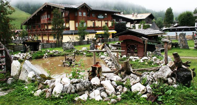 Estructura de madera y estanque con piedras y vegetación en un entorno rural.