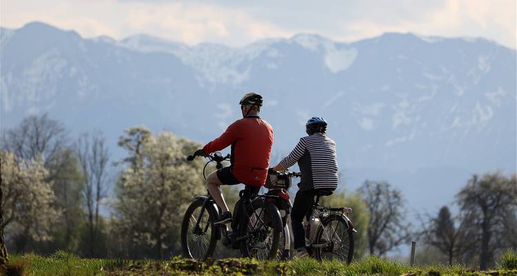 Deux personnes faisant du vélo avec en toile de fond des montagnes enneigées.