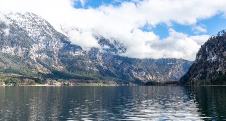 Un lac avec des reflets de montagnes enneigées et de nuages.