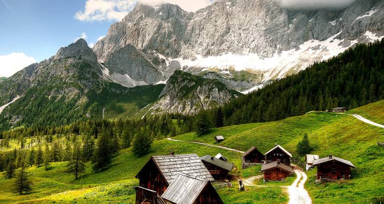 Rustic alpine village in a lush green valley with mountains.