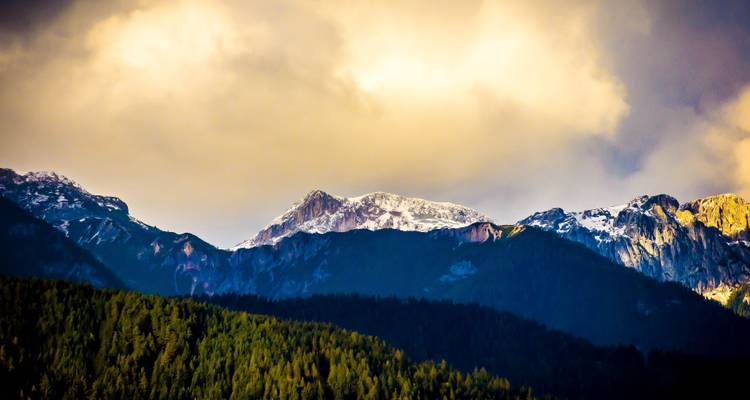 Mountain range with dramatic lighting under a cloudy sky.