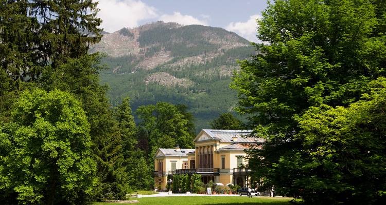 Villa jaune avec des arbres et une montagne en arrière-plan.