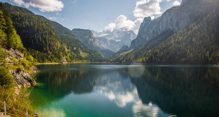 Lac de montagne entouré de hauts sommets et de forêt.