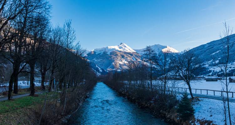 Rivière coulant entre des paysages saupoudrés de neige avec un arrière-plan de montagnes.