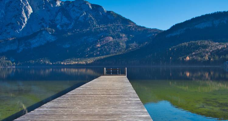 Wooden dock extending into a clear lake with mountains.