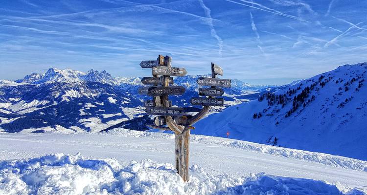 Schneebedeckte Berge mit einem hölzernen Wegweiser, der Richtungen anzeigt.