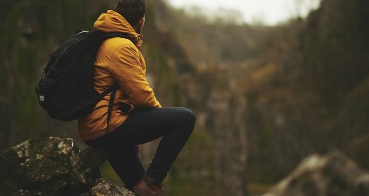 Eine Person, die auf einem Felsen sitzt und über ein malerisches Tal blickt.