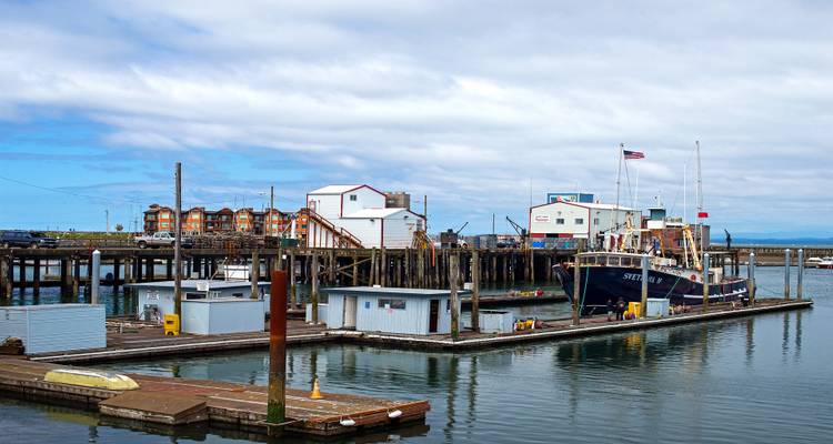 Pequeño puerto con barcos de pesca, muelles de madera y cobertizos bajo un cielo parcialmente nublado.