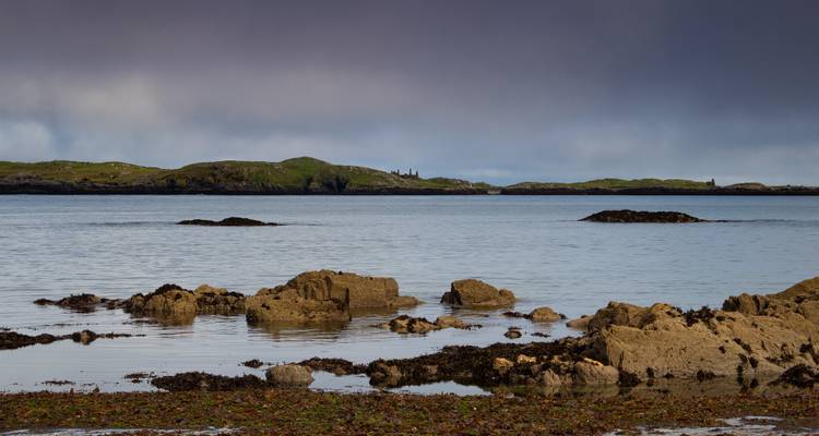 Orilla rocosa e islas bajas lejanas bajo un cielo gris y nublado.