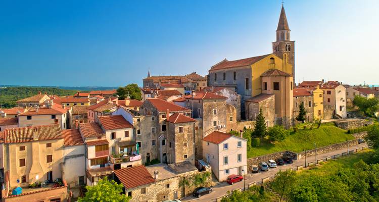 Vue rapprochée de vieux bâtiments en pierre avec un clocher d'église dans un soleil couchant chaleureux.