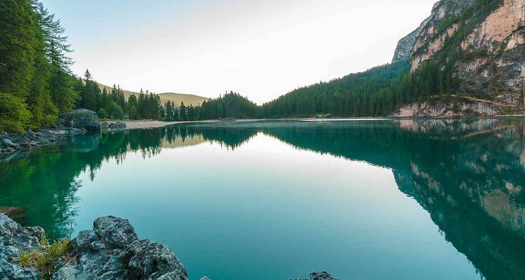 Lac tranquille reflétant les forêts environnantes et les collines à l'aube.