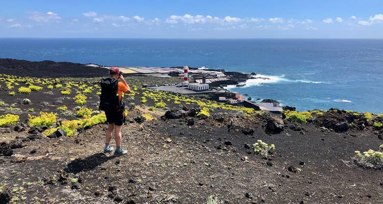 Vue sur un paysage volcanique vers l'océan avec un phare en vue.