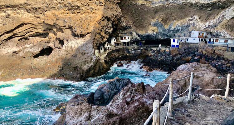 Cavernes côtières avec une eau bleue agitée s'étendant vers de petites structures construites dans la roche.